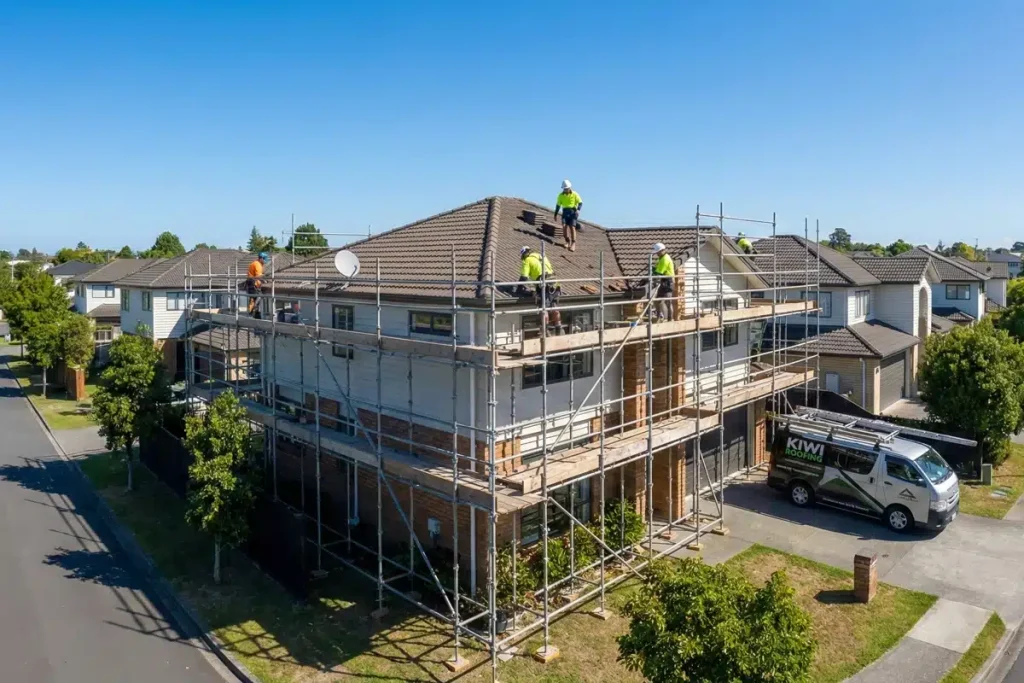 Aerial view of construction workers on scaffolding performing roof and exterior work on a two-story residential home in a suburban neighborhood.